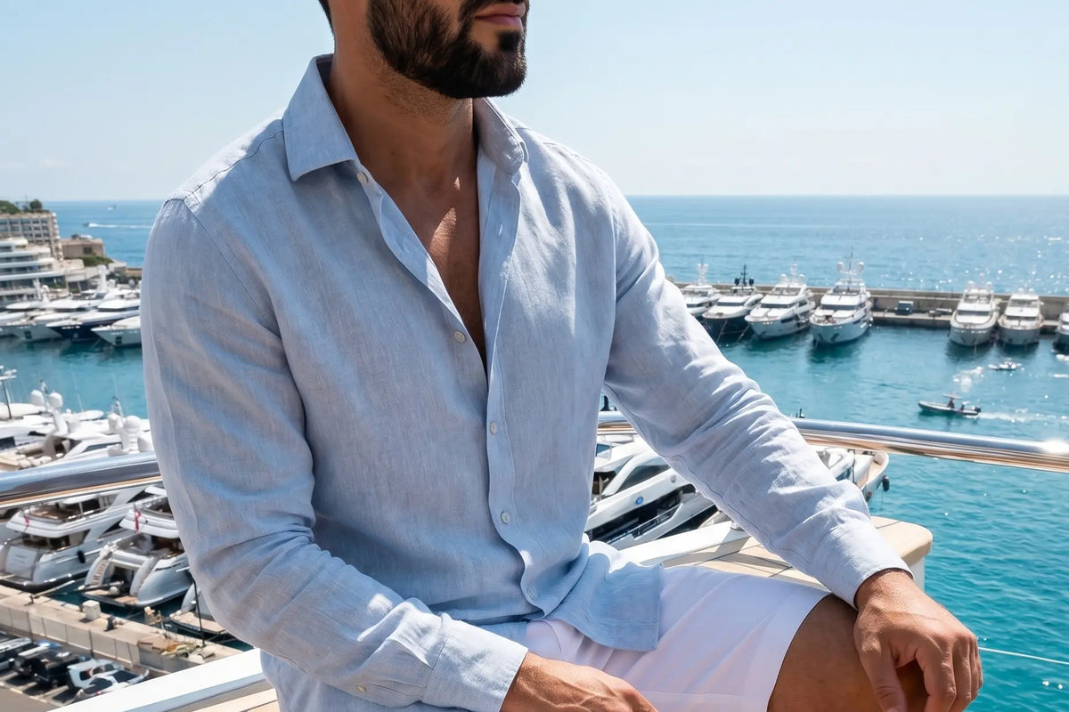 Homme assis en chemise de lin bleu clair, manches retroussées, face à la mer
